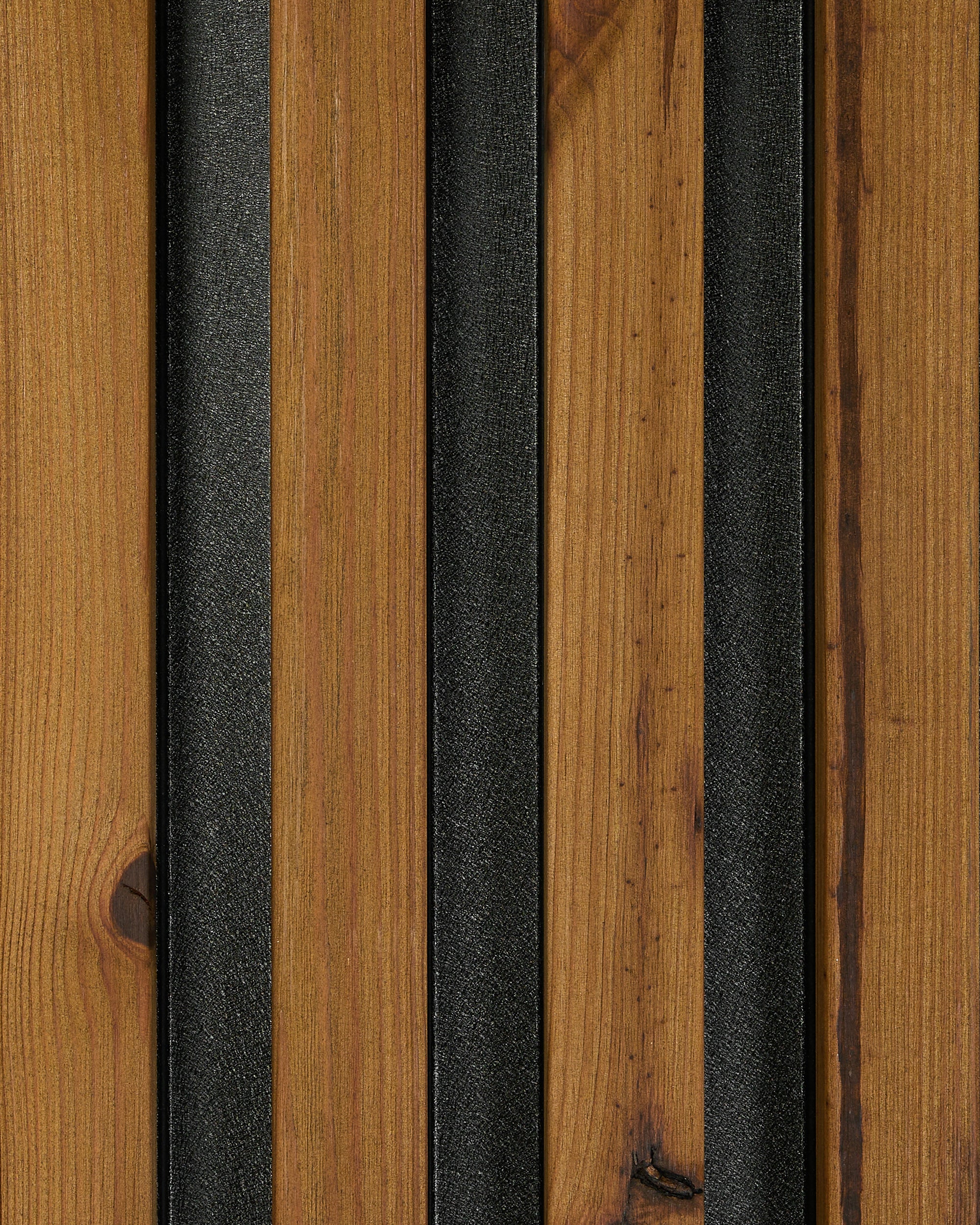 Close-up of vertical brown Akupanel acoustic wood slats with dark black metal strips, showing the Nordic-inspired industrial detail of WoodUpps panel design.